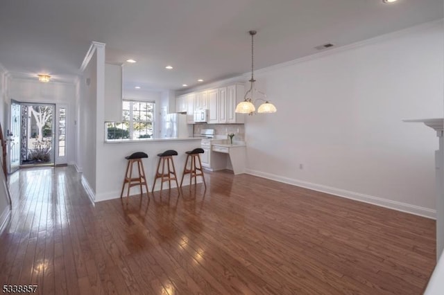 kitchen with white appliances, baseboards, a breakfast bar area, hardwood / wood-style floors, and a peninsula