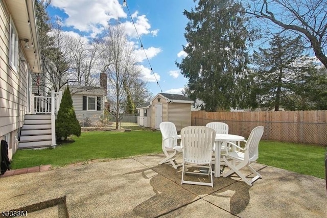 view of patio / terrace with an outbuilding, outdoor dining area, a fenced backyard, and a shed