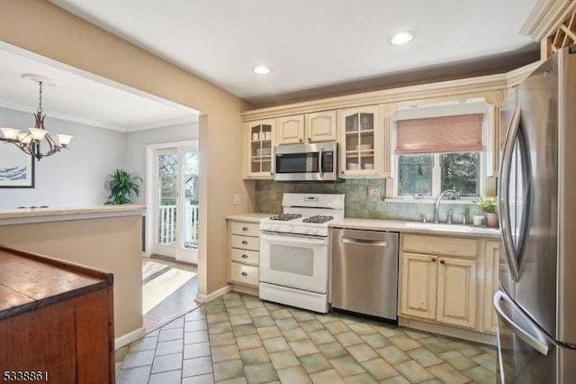 kitchen with light countertops, backsplash, appliances with stainless steel finishes, glass insert cabinets, and a sink