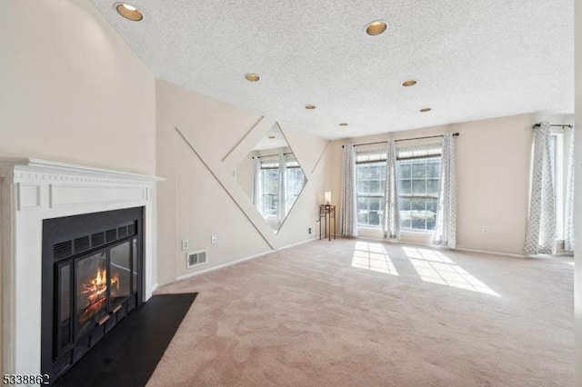 unfurnished living room with a fireplace with flush hearth, visible vents, light carpet, and a textured ceiling