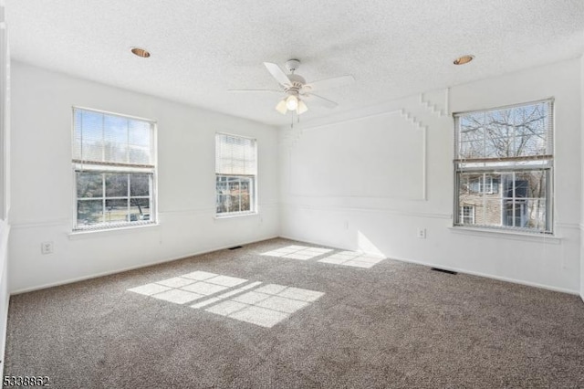 empty room featuring visible vents, carpet flooring, ceiling fan, and a textured ceiling