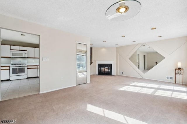 unfurnished living room with a textured ceiling, light carpet, visible vents, baseboards, and a glass covered fireplace