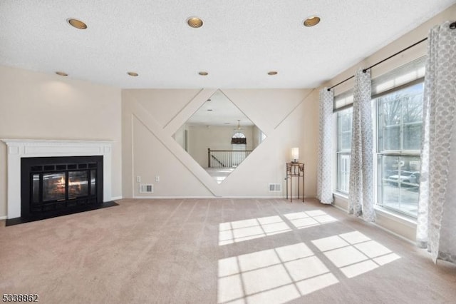 unfurnished living room with light carpet, a textured ceiling, a fireplace with flush hearth, and visible vents