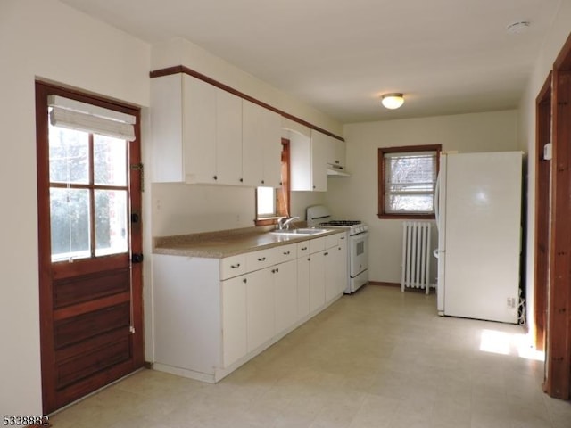 kitchen featuring white appliances, light countertops, radiator heating unit, and white cabinetry