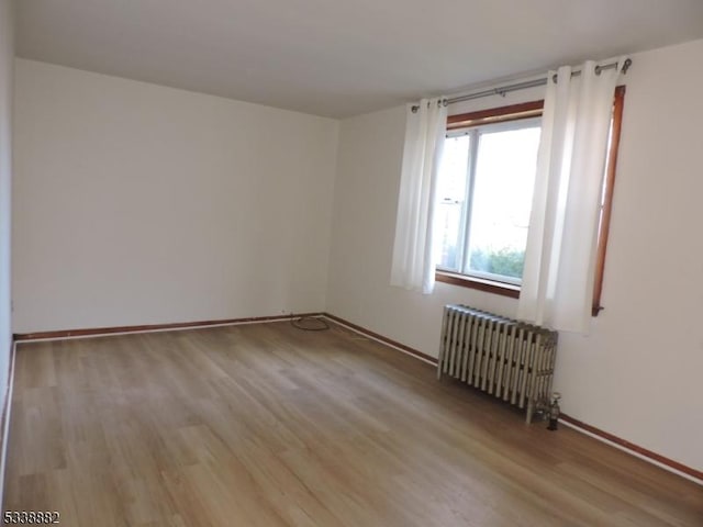 spare room with baseboards, light wood finished floors, and radiator