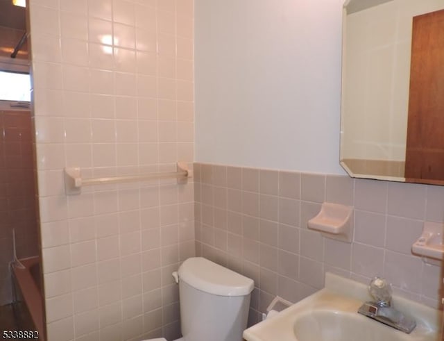 bathroom featuring toilet, a sink, and tile walls