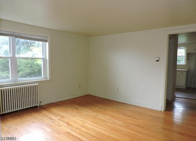 spare room featuring light wood finished floors, radiator heating unit, and baseboards