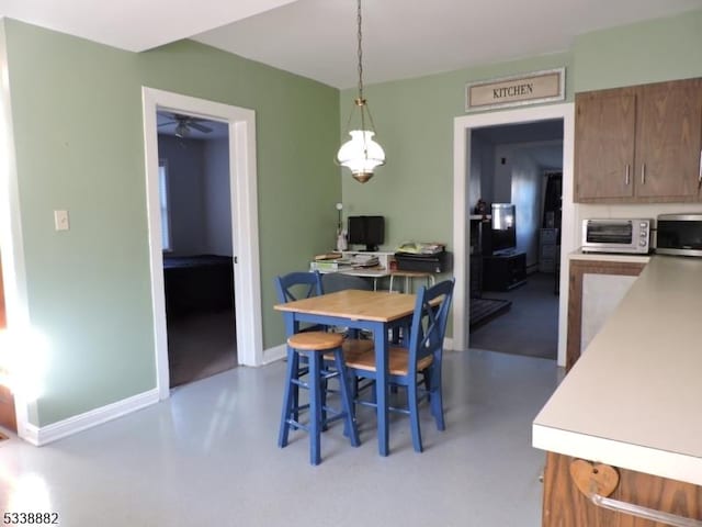 dining area with concrete flooring, a toaster, baseboards, and a ceiling fan