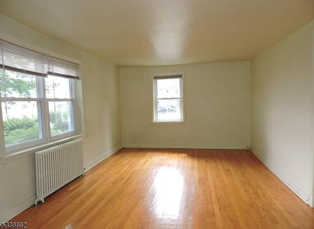 spare room featuring radiator heating unit, light wood-style flooring, and baseboards