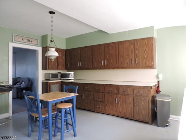 kitchen featuring finished concrete floors, light countertops, hanging light fixtures, and baseboards