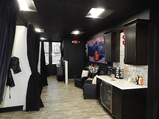 cinema room featuring light wood finished floors, wine cooler, a paneled ceiling, and a dry bar