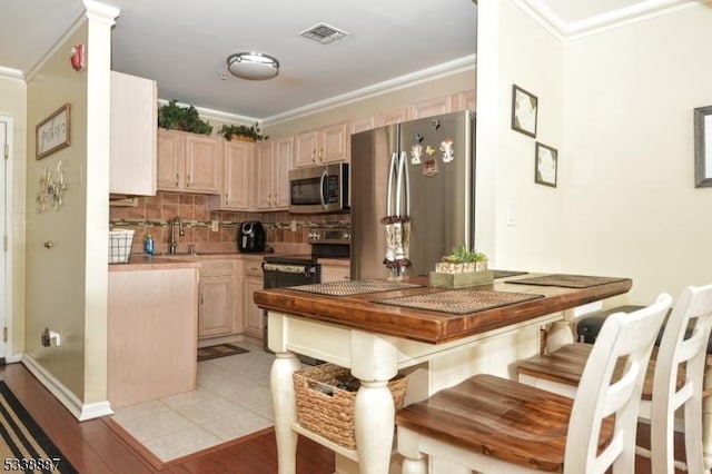 kitchen with ornamental molding, appliances with stainless steel finishes, light brown cabinets, and backsplash