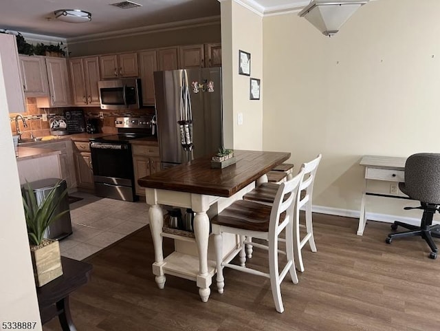 kitchen featuring appliances with stainless steel finishes, tasteful backsplash, light wood-type flooring, ornamental molding, and sink