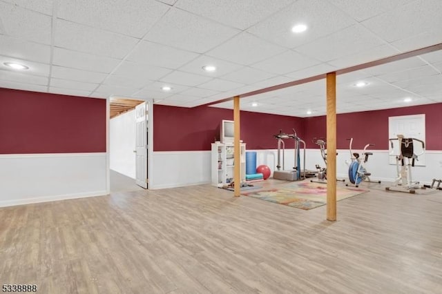 finished basement featuring a paneled ceiling, a wainscoted wall, recessed lighting, and wood finished floors