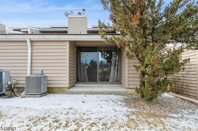 snow covered house featuring a chimney and cooling unit