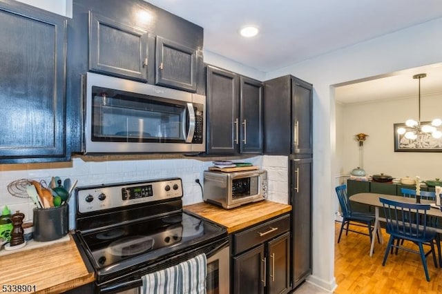 kitchen featuring light wood finished floors, an inviting chandelier, stainless steel appliances, pendant lighting, and backsplash