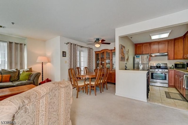 kitchen featuring stainless steel appliances, light colored carpet, brown cabinetry, open floor plan, and under cabinet range hood