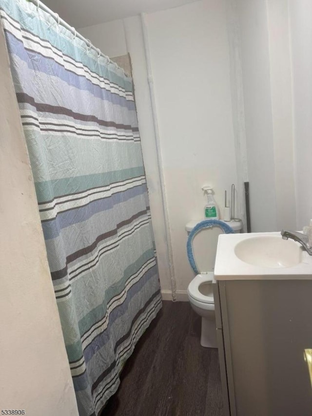 bathroom featuring baseboards, a shower with shower curtain, toilet, wood finished floors, and vanity