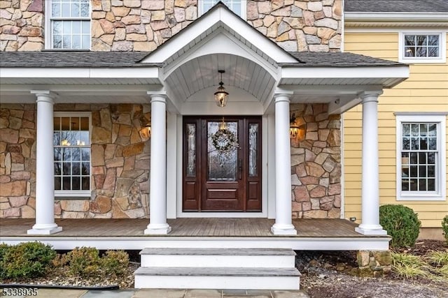 view of exterior entry featuring covered porch, a shingled roof, and stone siding