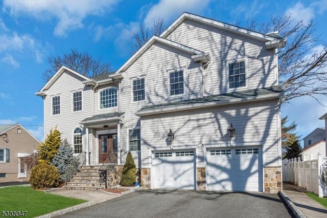 traditional-style house with aphalt driveway, stone siding, fence, and an attached garage