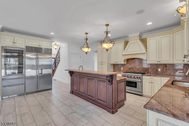 kitchen with custom range hood, high quality appliances, a center island, cream cabinetry, and pendant lighting