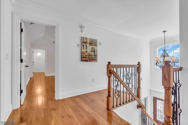 hall featuring a notable chandelier, light wood-style floors, ornamental molding, an upstairs landing, and baseboards