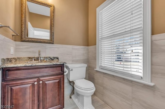 half bathroom featuring toilet, wainscoting, tile walls, and vanity