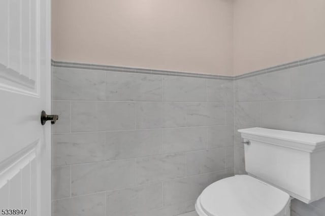 bathroom with a wainscoted wall, toilet, and tile walls