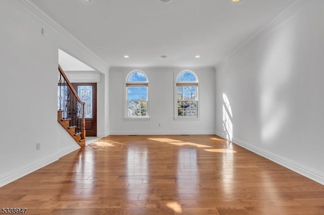 unfurnished living room featuring light wood-style floors, crown molding, baseboards, and stairs