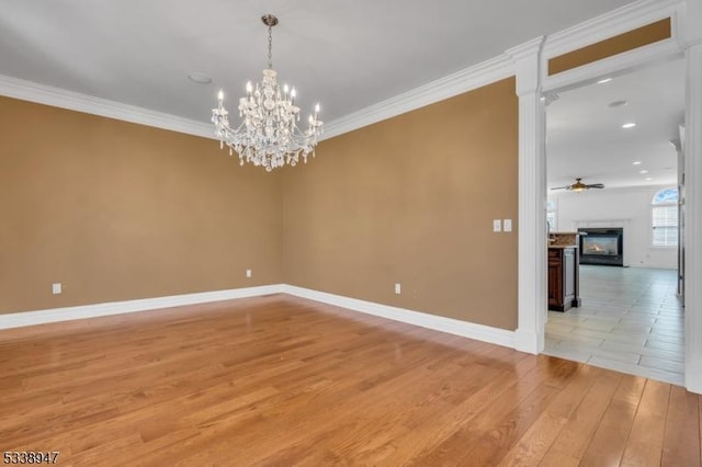 empty room featuring light wood finished floors, ornamental molding, a glass covered fireplace, and ceiling fan with notable chandelier