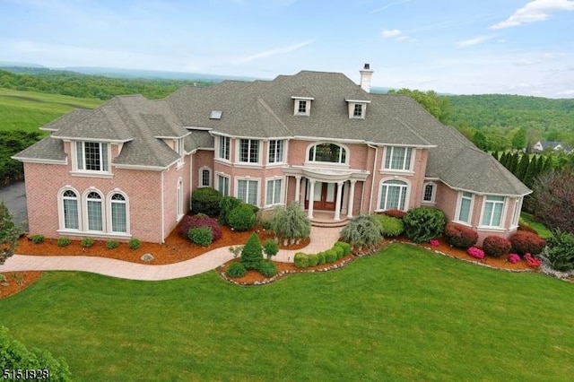 georgian-style home with a shingled roof, brick siding, a chimney, and a front lawn