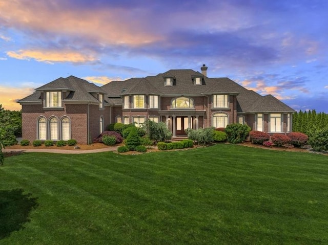 view of front of property featuring brick siding, a chimney, and a front yard