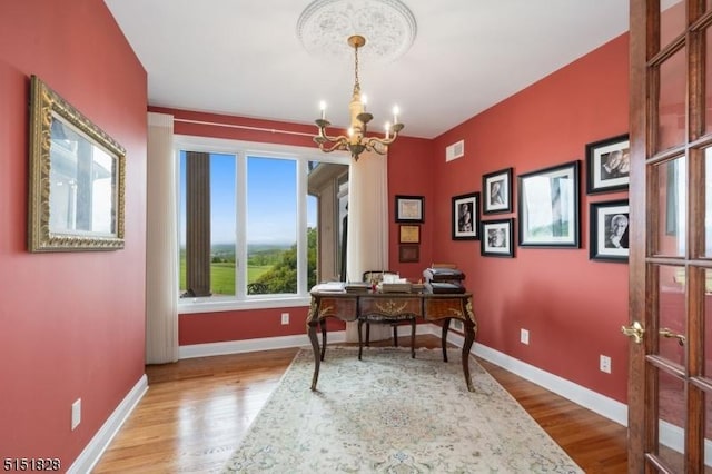 office space with an inviting chandelier, visible vents, baseboards, and wood finished floors