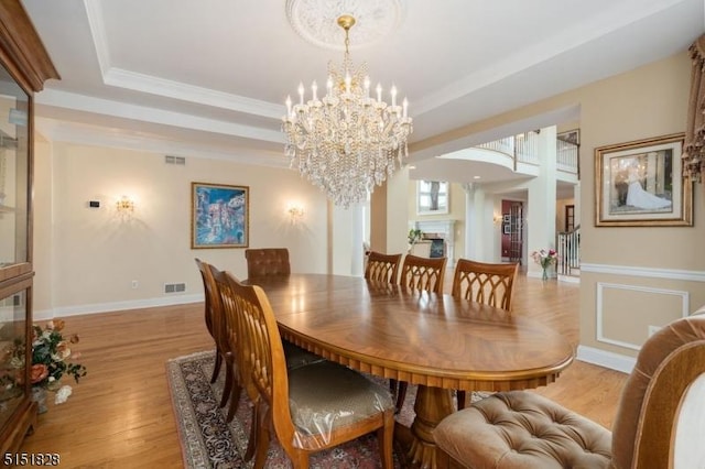 dining area with a fireplace, a raised ceiling, visible vents, an inviting chandelier, and light wood-style floors