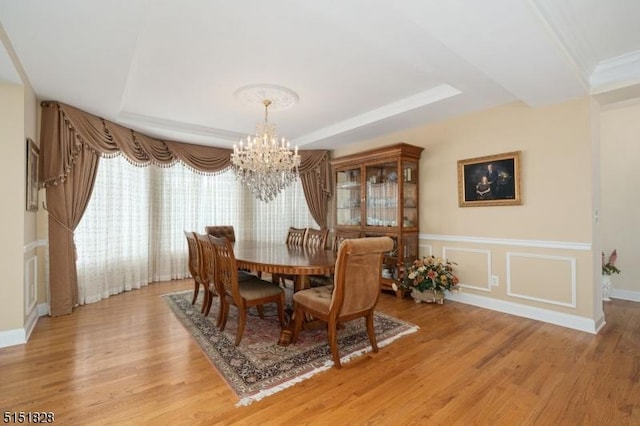 dining space featuring a tray ceiling, a decorative wall, light wood-style flooring, and an inviting chandelier