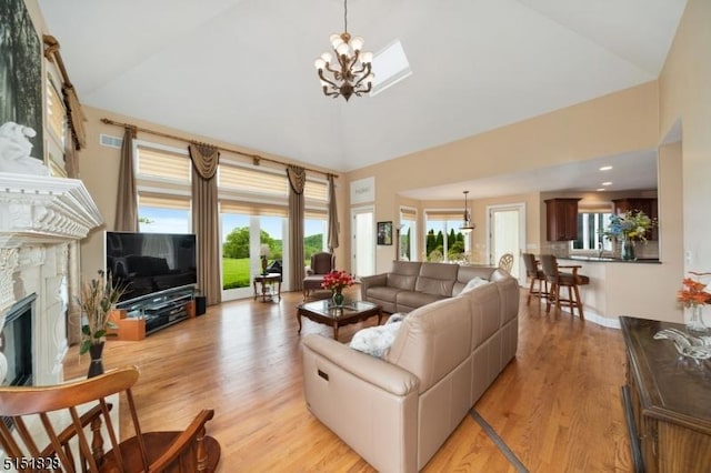 living room featuring high vaulted ceiling, light wood finished floors, a glass covered fireplace, and an inviting chandelier