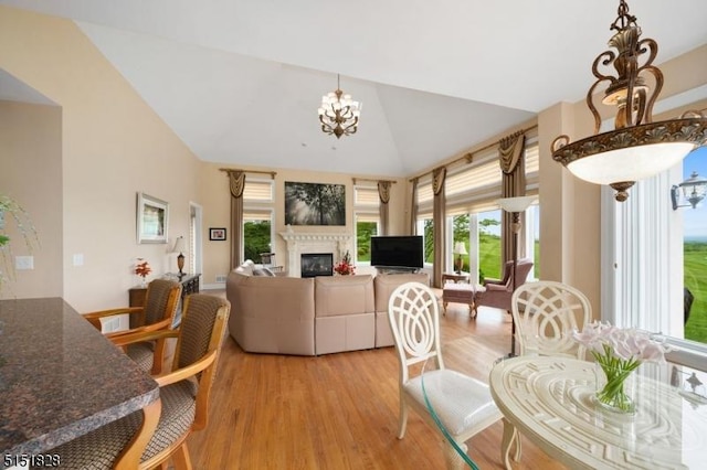 dining room featuring light wood-type flooring, an inviting chandelier, lofted ceiling, and a glass covered fireplace