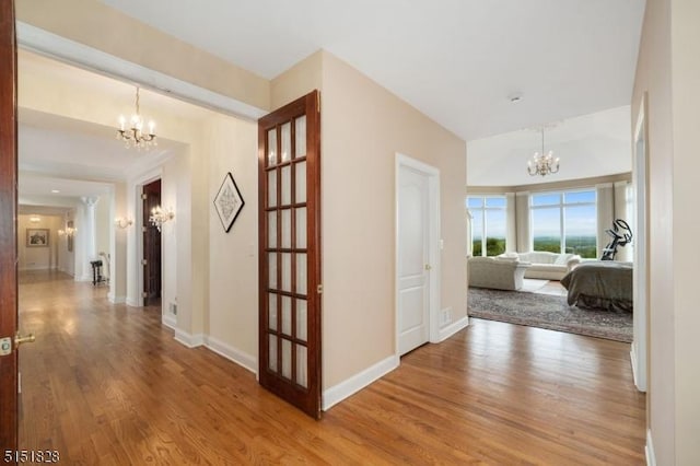 hallway with baseboards, wood finished floors, and a notable chandelier