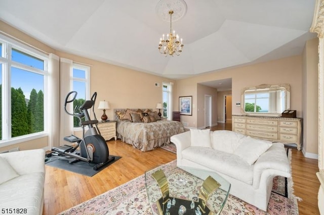 bedroom featuring a chandelier, lofted ceiling, baseboards, light wood-type flooring, and a raised ceiling