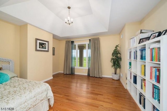 bedroom with light wood-type flooring, baseboards, a raised ceiling, and a chandelier