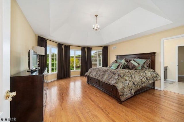 bedroom with light wood finished floors, a raised ceiling, visible vents, an inviting chandelier, and baseboards