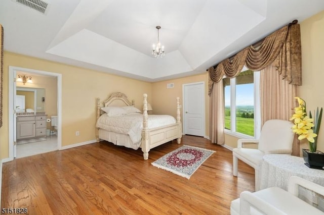 bedroom with baseboards, visible vents, wood finished floors, a tray ceiling, and a notable chandelier