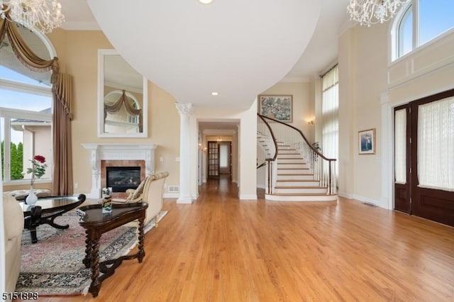 foyer entrance featuring a wealth of natural light, an inviting chandelier, a glass covered fireplace, light wood-type flooring, and stairs