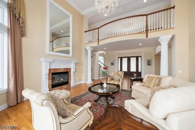 living area with ornamental molding, a tile fireplace, ornate columns, and wood finished floors