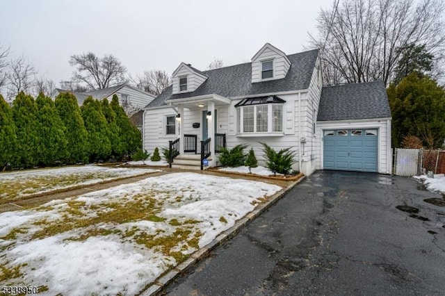 cape cod-style house featuring driveway, an attached garage, fence, and roof with shingles