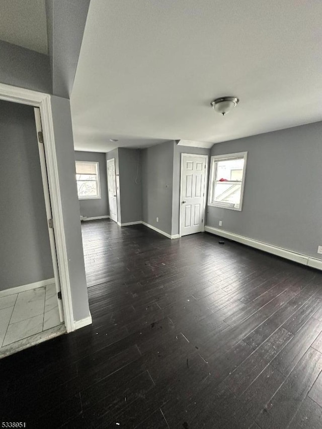 unfurnished room with a healthy amount of sunlight, dark wood-type flooring, and a baseboard heating unit