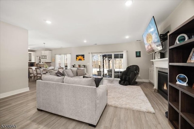 living area with recessed lighting, a lit fireplace, baseboards, and wood finished floors