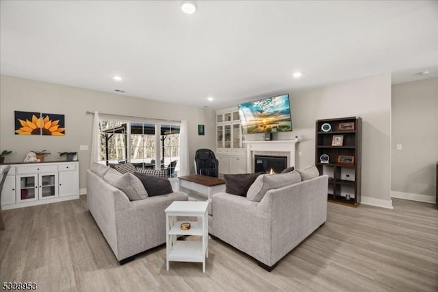 living room with a glass covered fireplace, baseboards, light wood finished floors, and recessed lighting