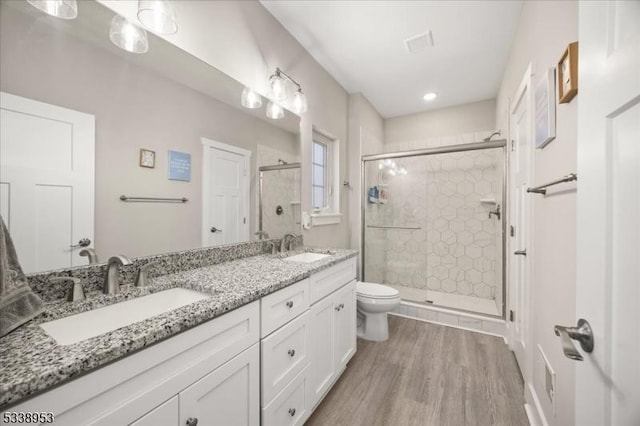 bathroom with toilet, wood finished floors, a sink, a shower stall, and double vanity