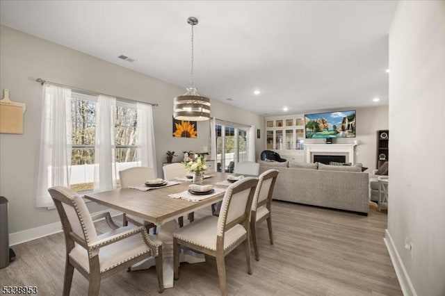 dining room featuring light wood finished floors, a fireplace, visible vents, and baseboards